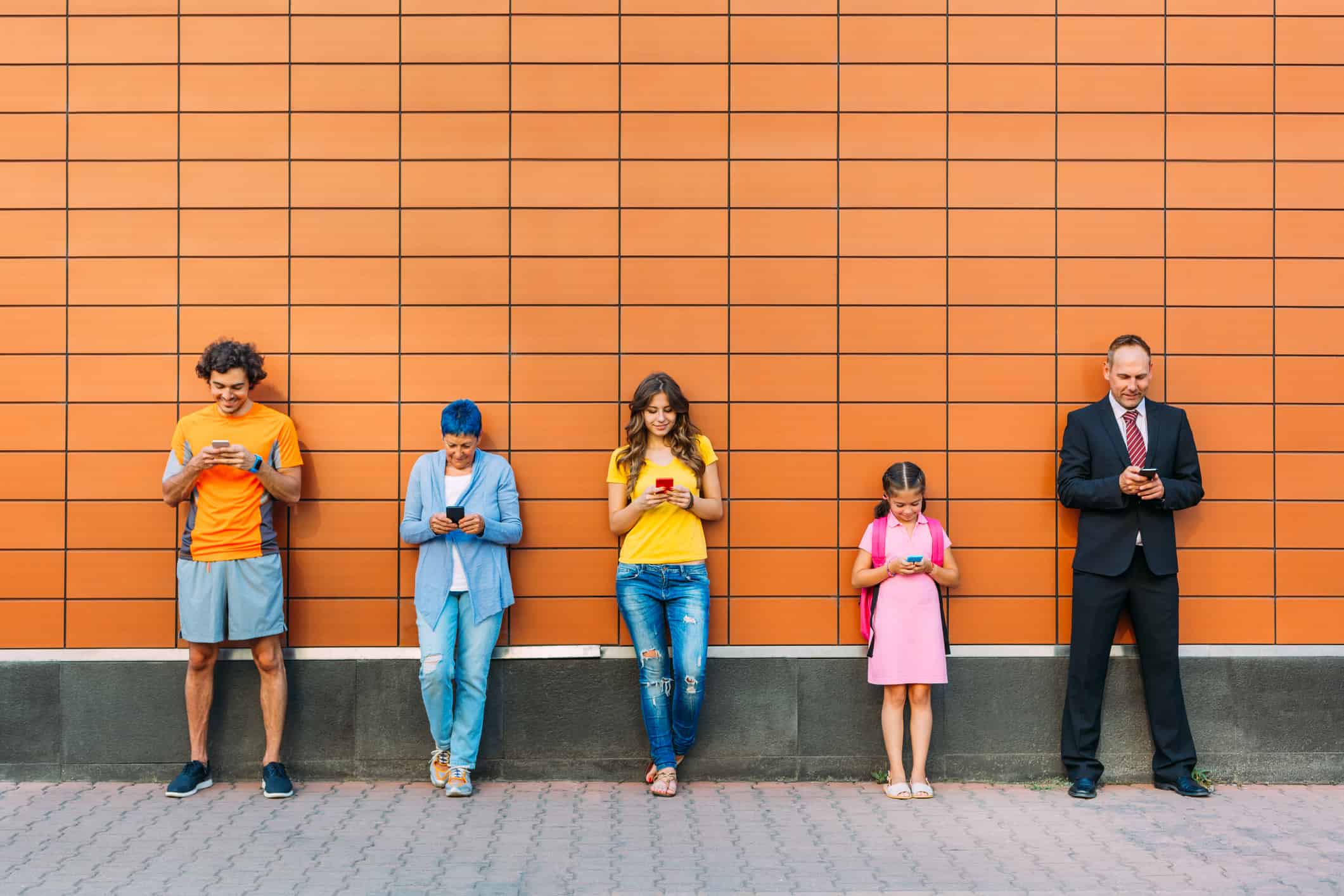 Group of different generation people standing against a wall and text messaging, social media and communication concept.